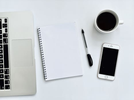 A clean and simple workspace featuring a laptop, smartphone, and coffee mug on a white desk.