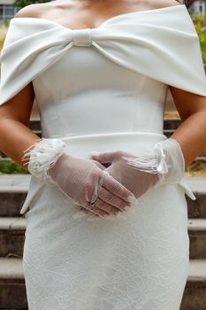 Close-up of a bride in a stylish white off-shoulder wedding dress and delicate lace gloves.