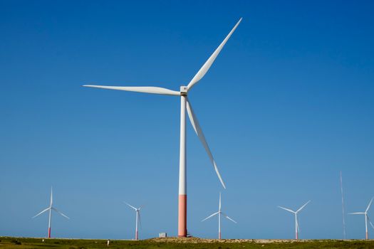 Large wind turbine in a green field with clear blue sky, showcasing renewable energy.