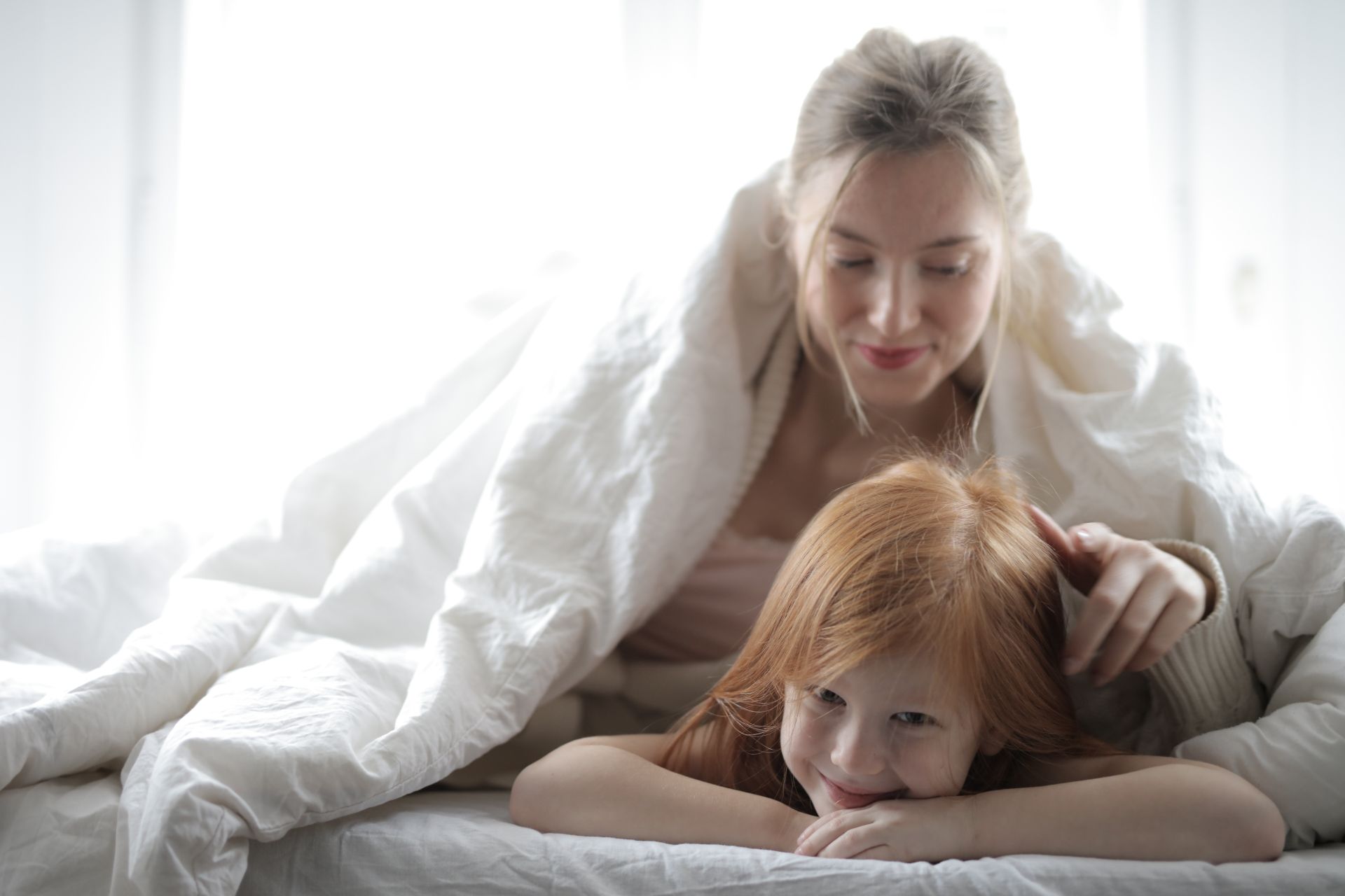 A joyful mother and daughter enjoy relaxing and bonding in bed, wrapped in a cozy blanket.
