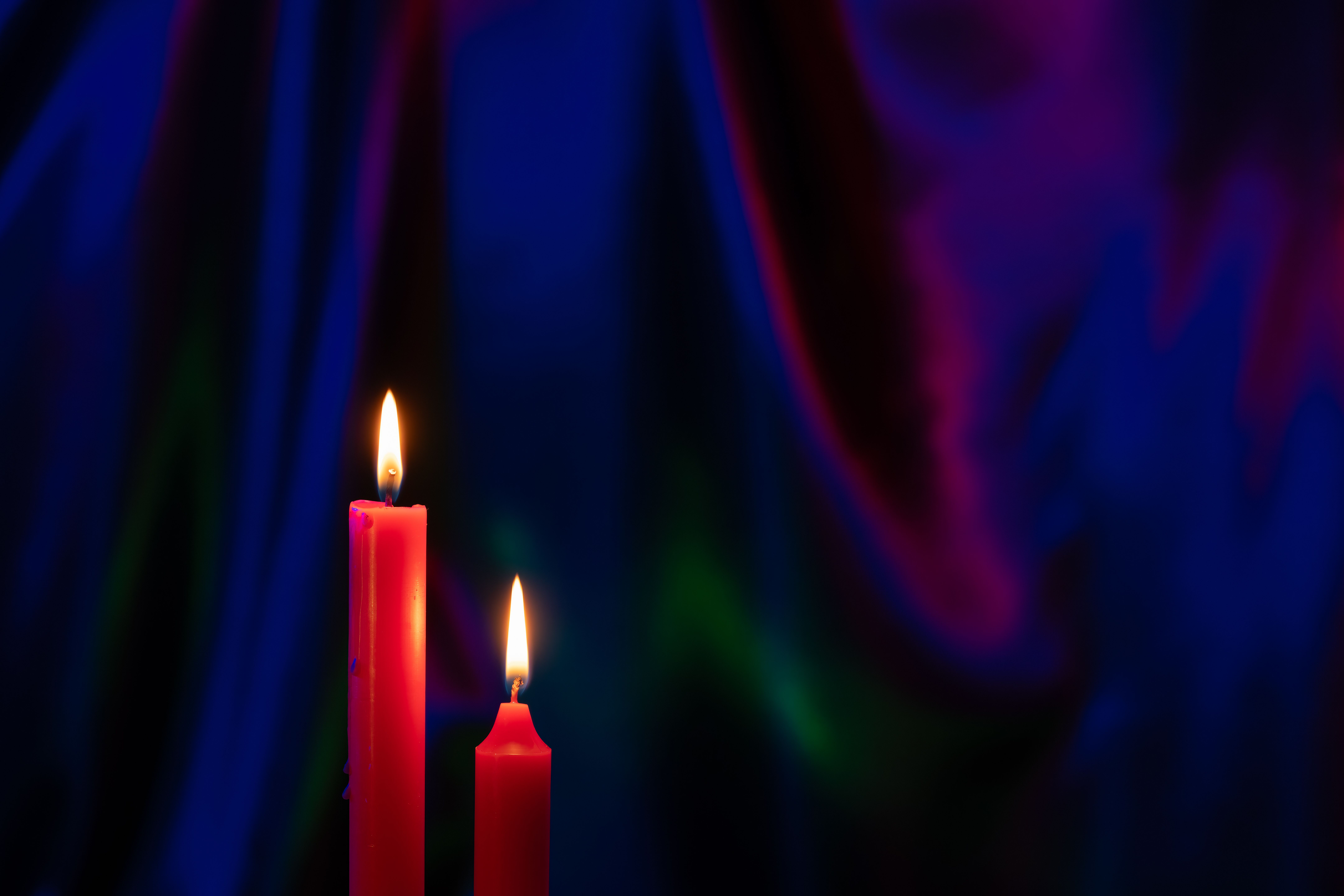 Fotomural Dos velas rojas con llamas vibrantes sobre un fondo de cortinas ricas y coloridas, creando una atmósfera cálida y acogedora.