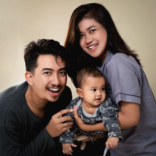 Free A joyful family portrait featuring smiling parents and their adorable baby in a warm setting. Stock Photo