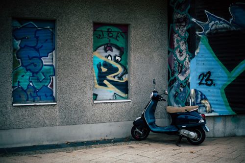 Free Blue scooter parked beside a wall with colorful graffiti art in an urban setting. Stock Photo