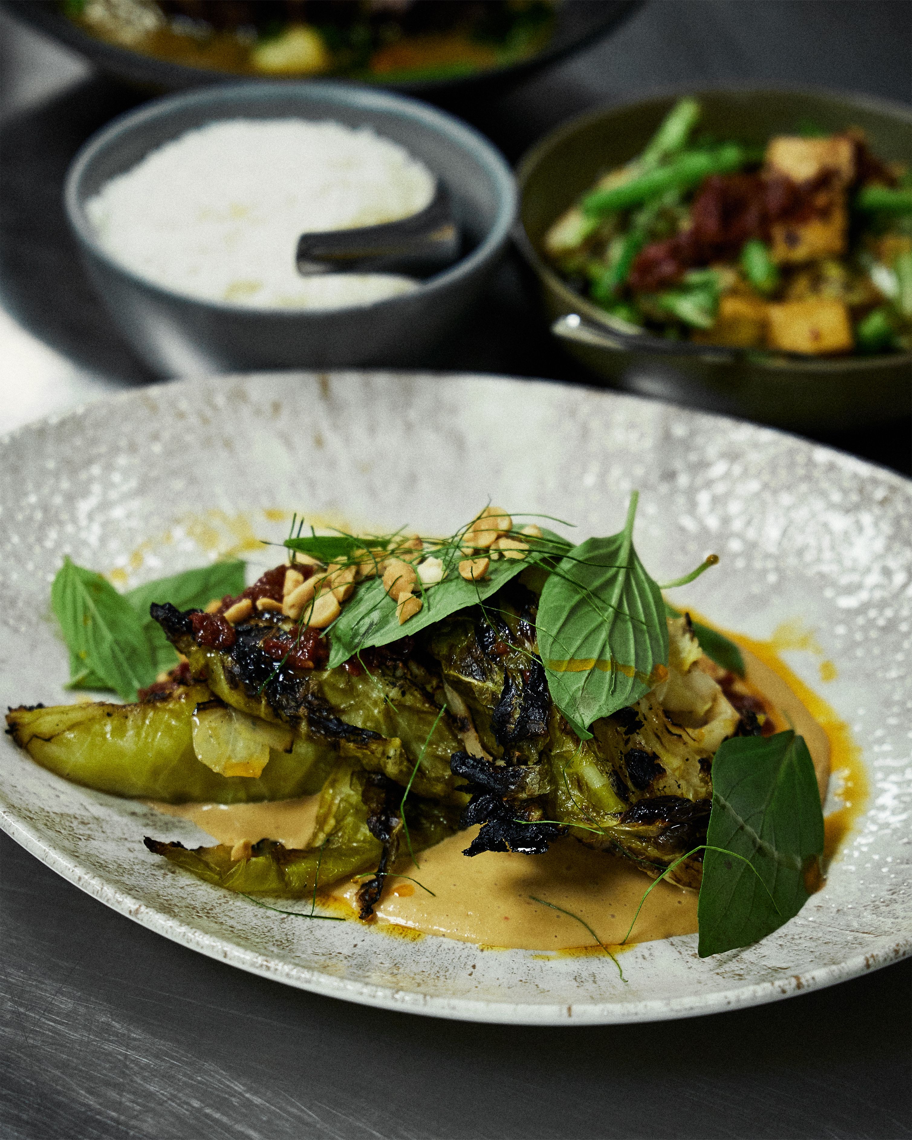 Grilled cabbage dish garnished with herbs and peanuts, served with a rich peanut sauce on a decorative white plate.