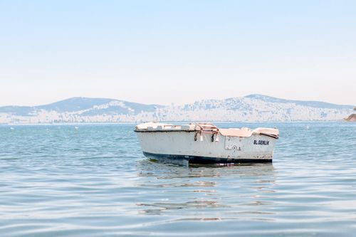 Free Solitary boat on serene water with distant city and hills in the background, under a clear sky. Stock Photo