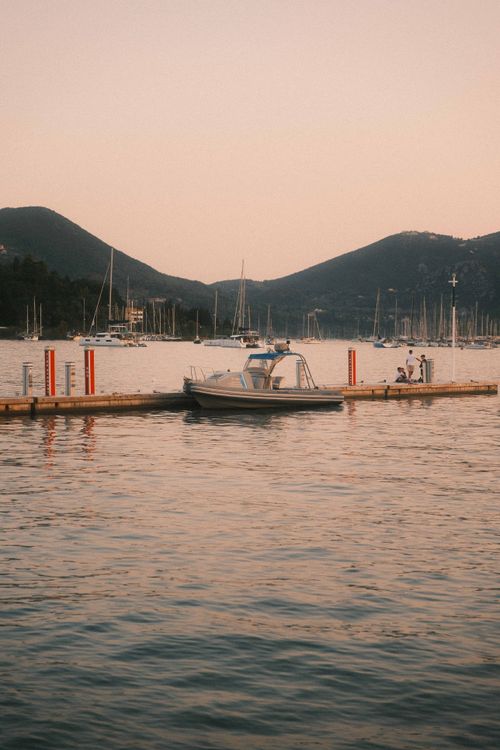 Free A serene scene of a boat at a marina dock against the backdrop of mountains and a warm sunset sky. Stock Photo