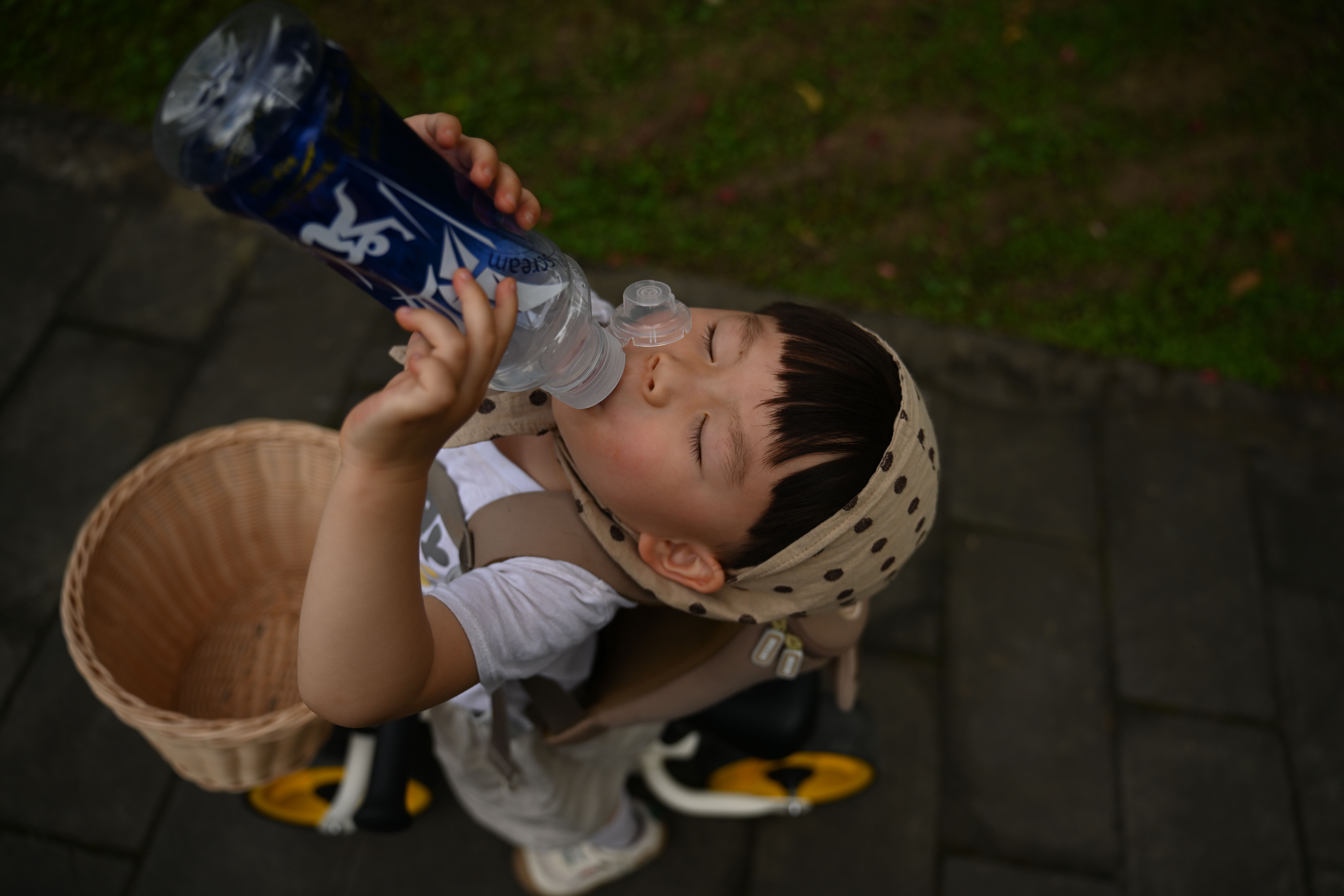 A young boy taking a refreshing water break while riding his tricycle outdoors.