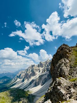 Breathtaking view of the rugged Dolomites under a bright blue sky with fluffy clouds.