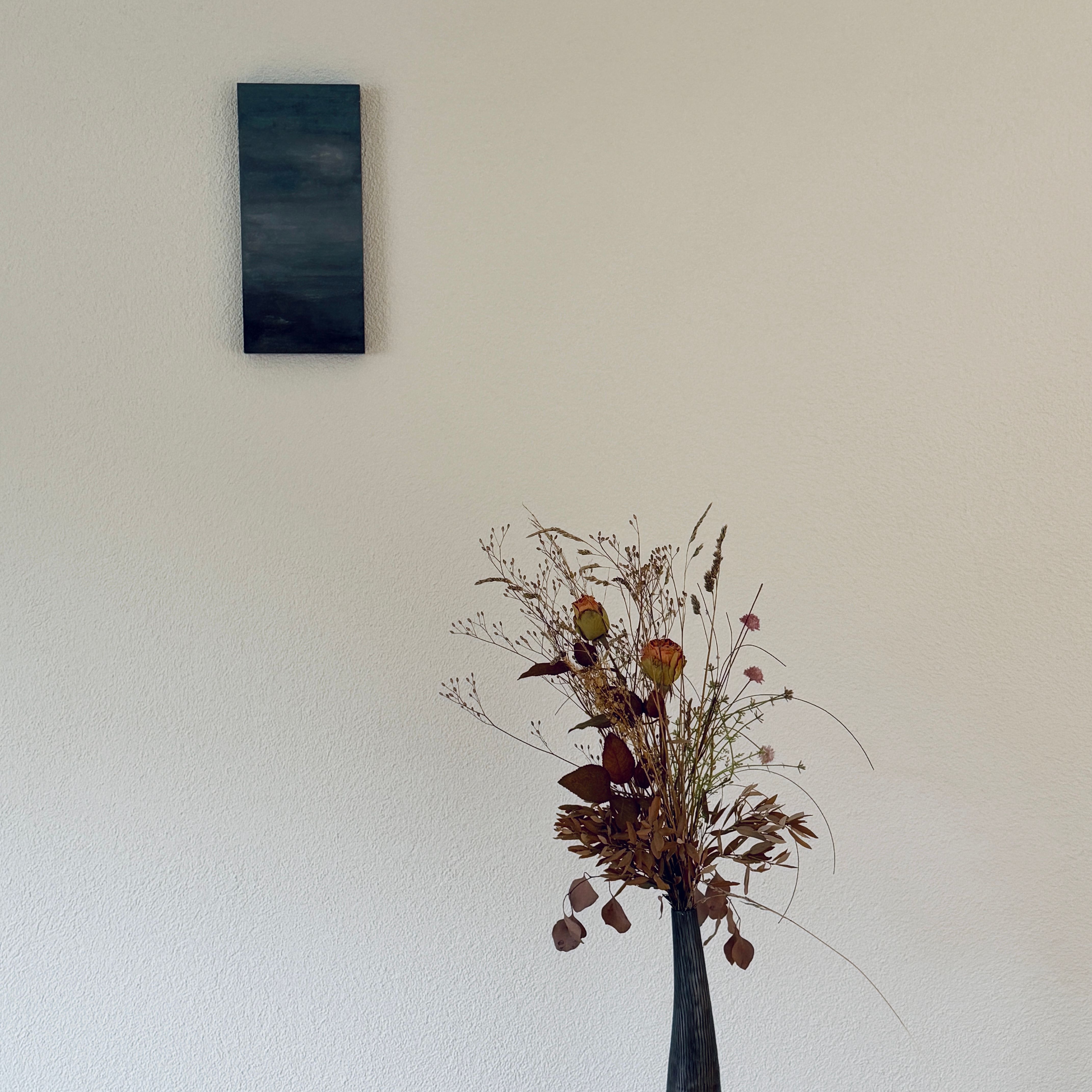 A minimalist interior with a focus on a dried floral arrangement in a vase against a neutral wall.