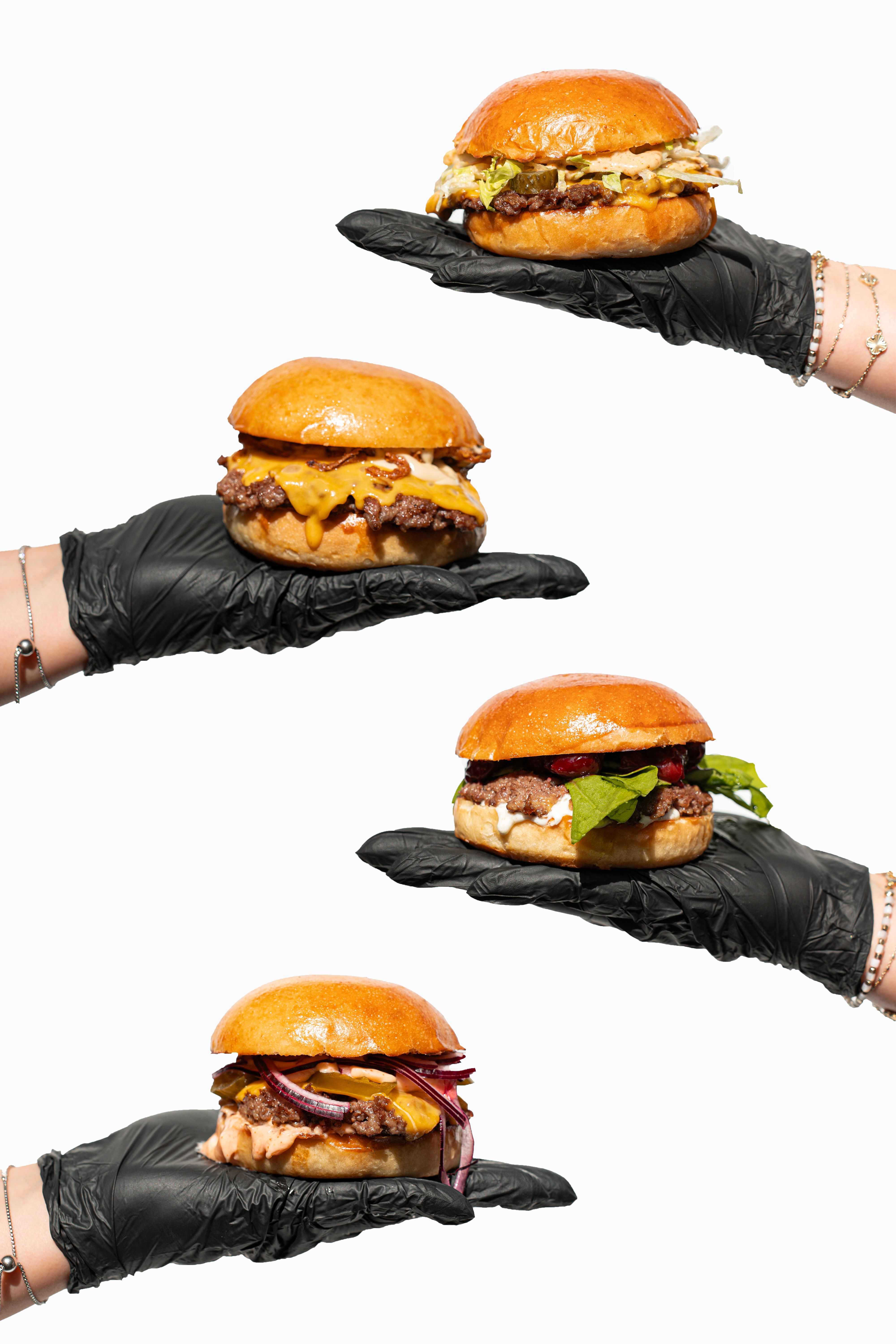 Four gourmet burgers presented on black-gloved hands isolated on a white background.