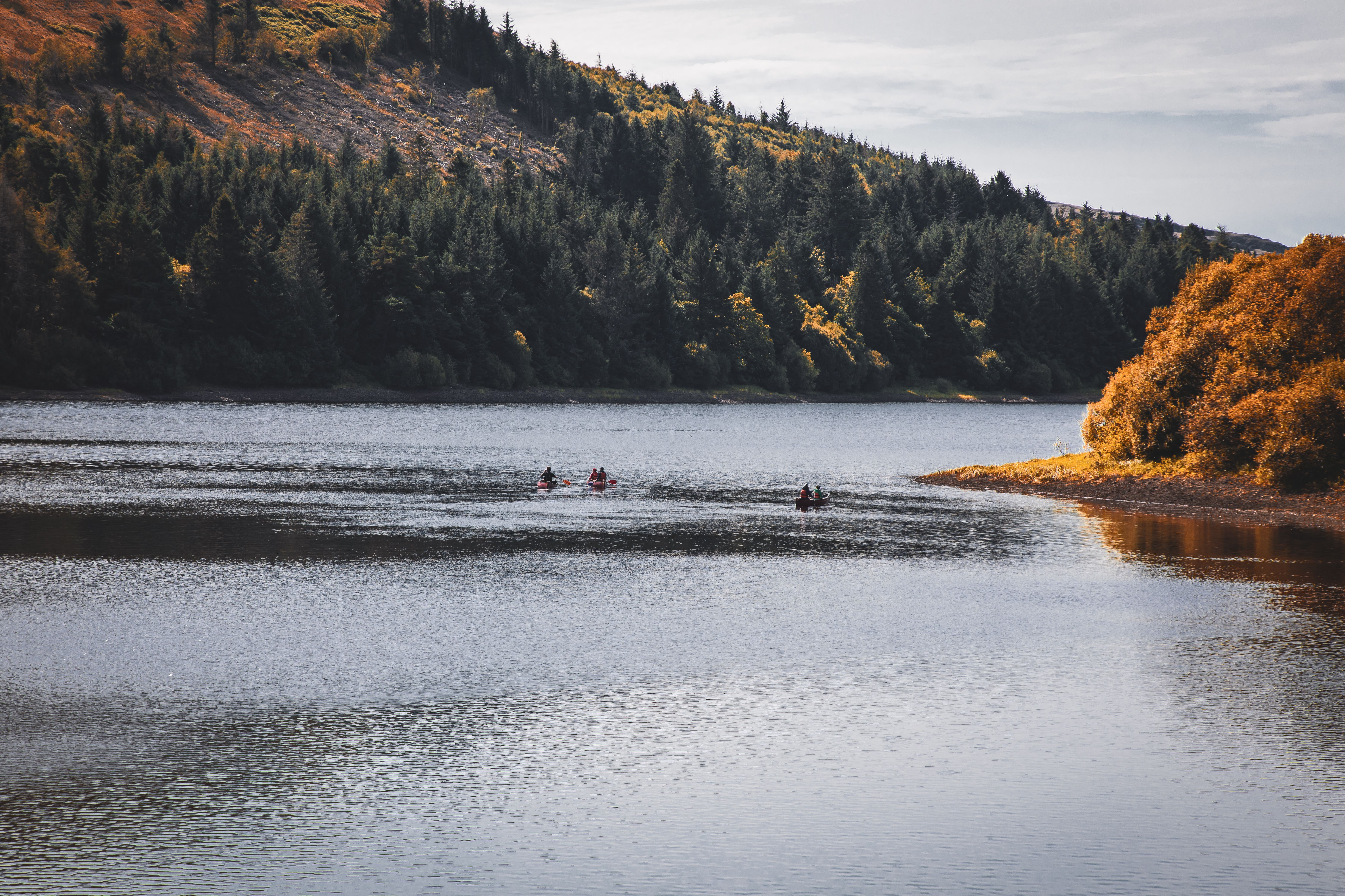 Canoe on a serene lake in Brecon Beacons, Wales with forested hills in fall colors.