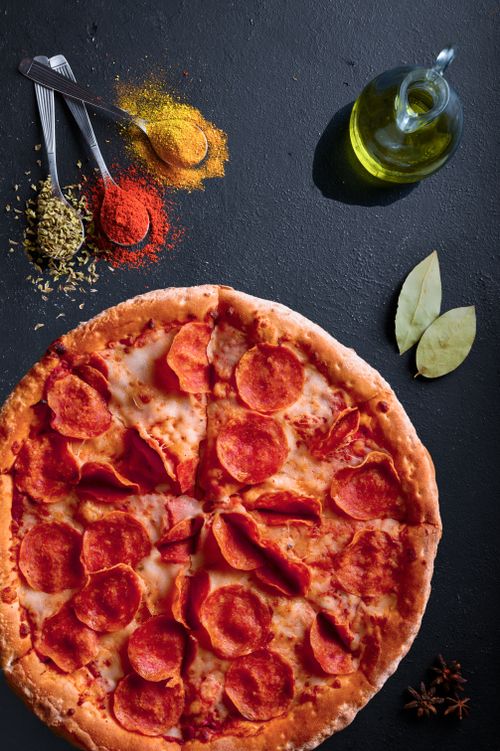 Free Freshly baked pepperoni pizza with a variety of spices on a dark surface. Stock Photo