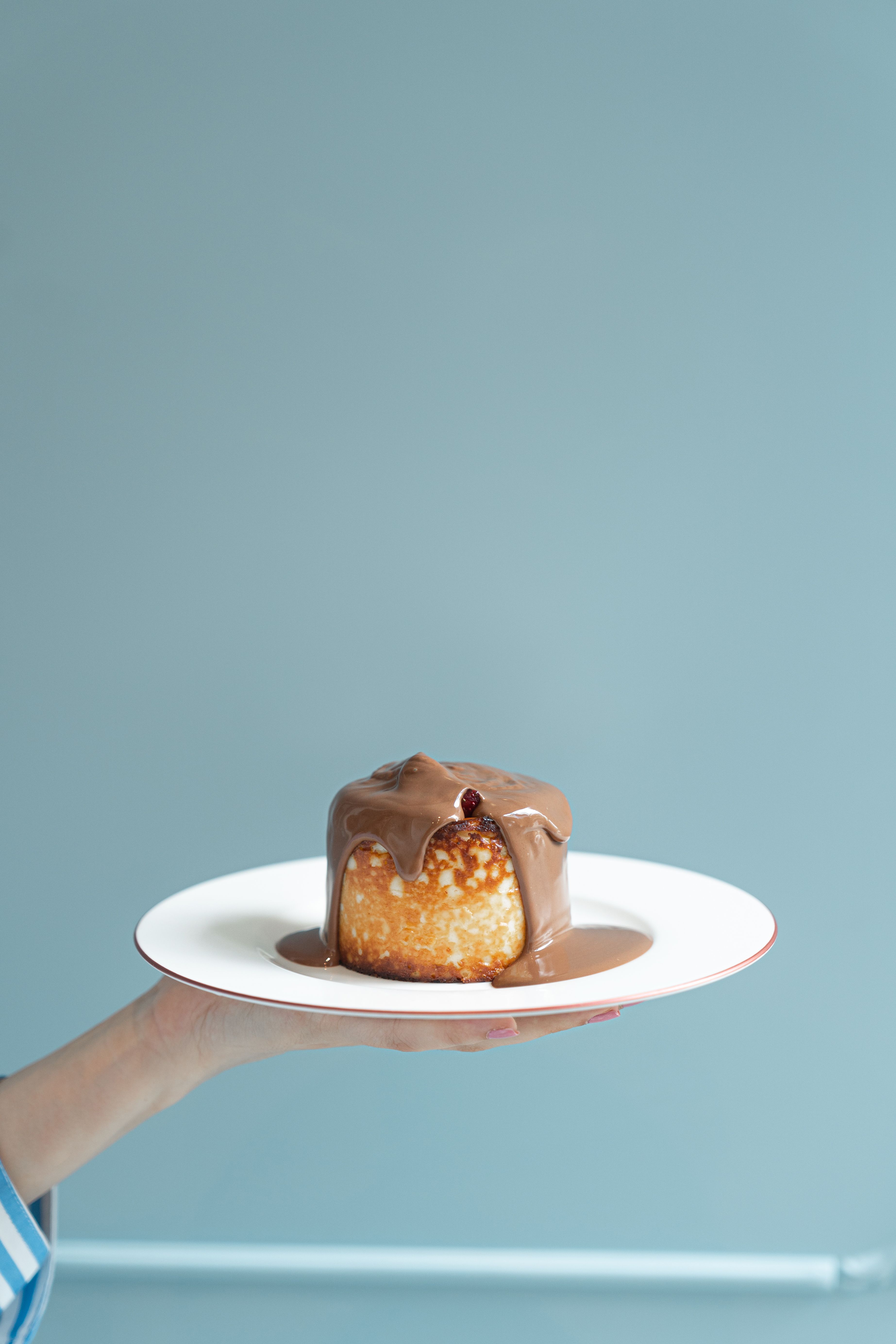 A decadent cheesecake topped with rich chocolate sauce against a soft blue background.