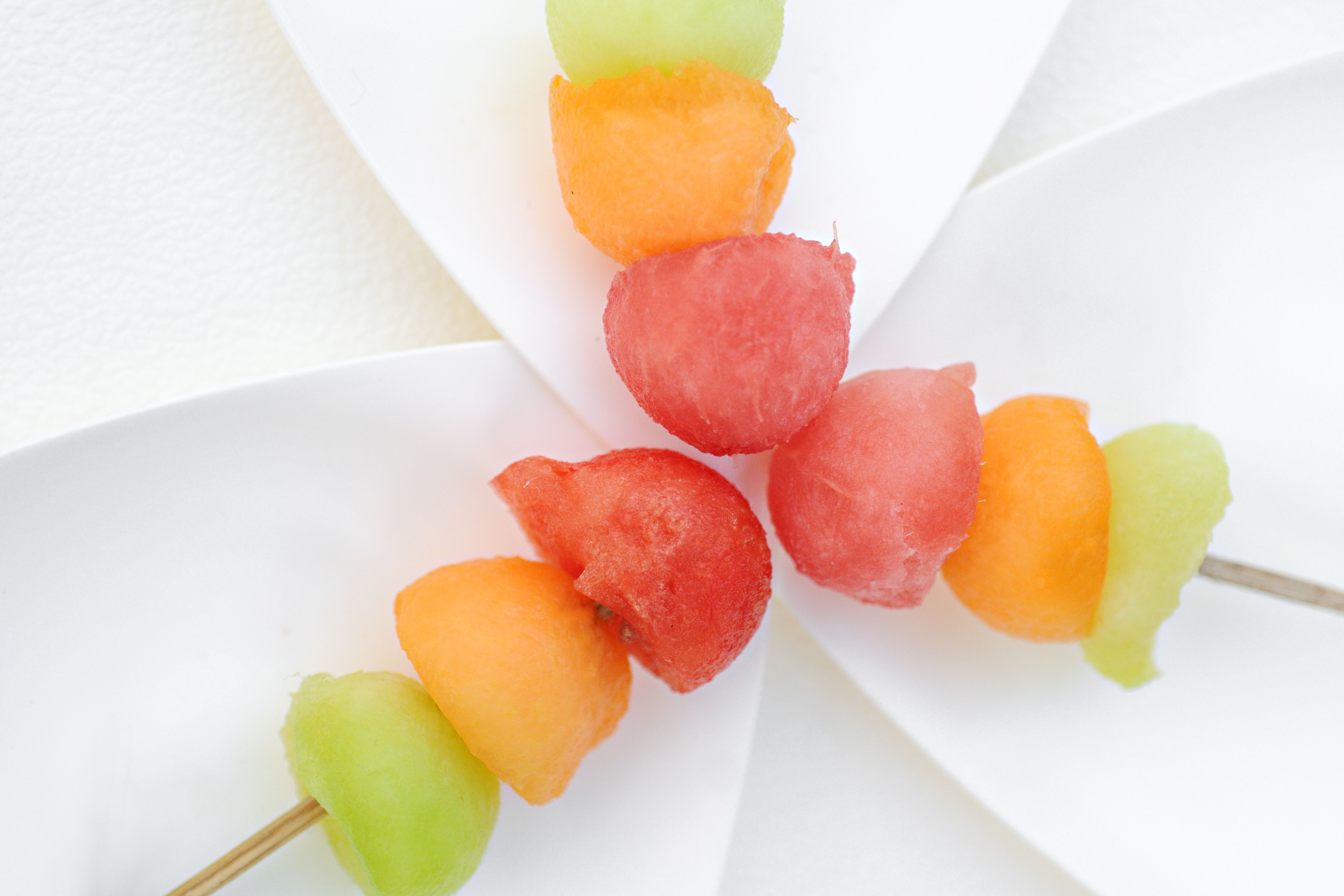 Fresh melon balls on skewers arranged on modern white plates.