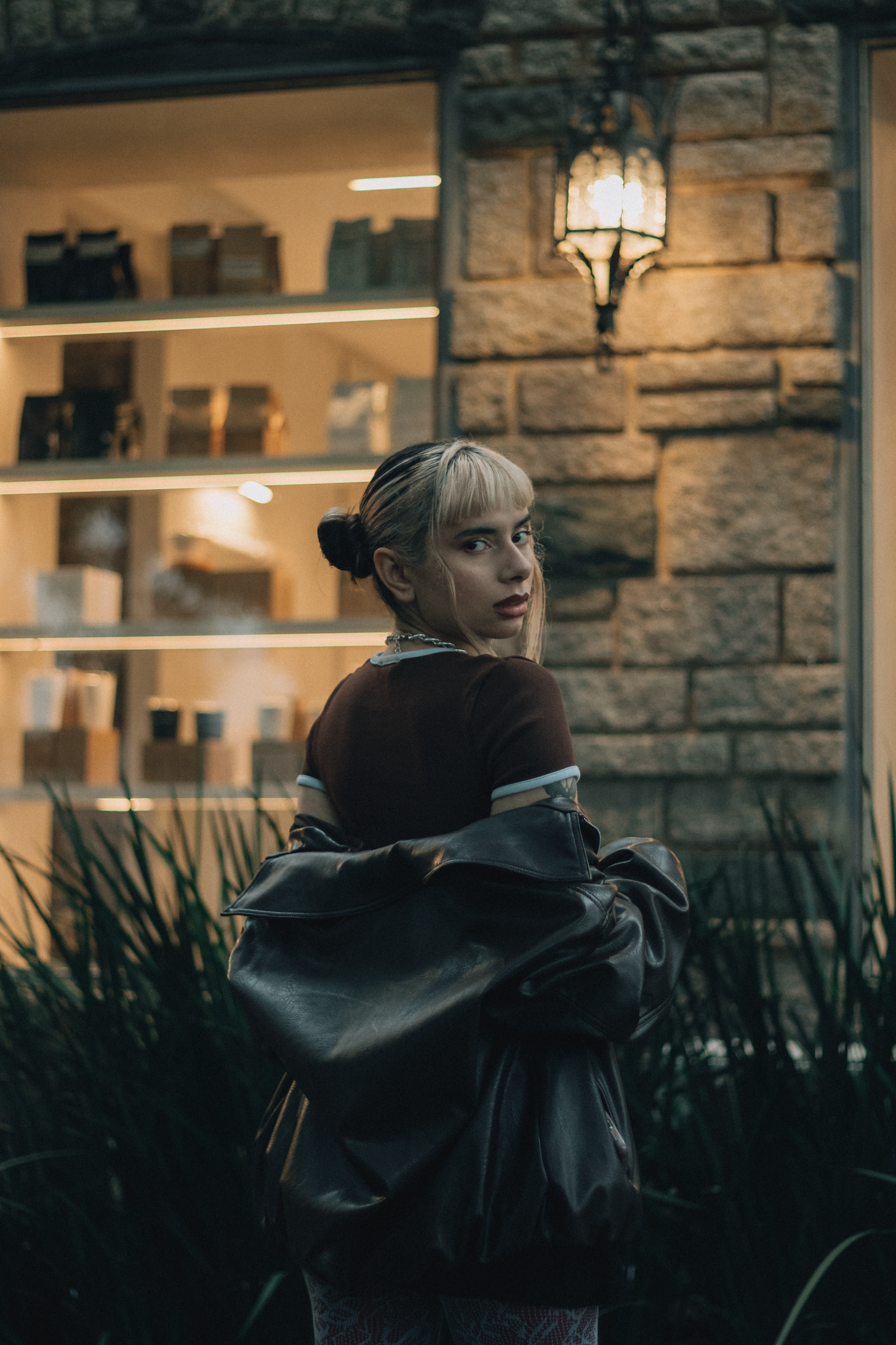 Fashionable woman posing outdoors at night by a charming illuminated shop.