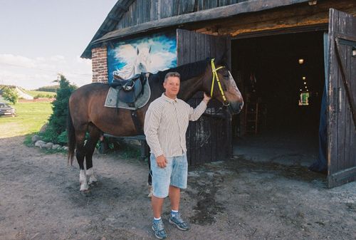 Free A man stands with a horse outside a barn in Smolevichi, Belarus on a sunny day. Stock Photo