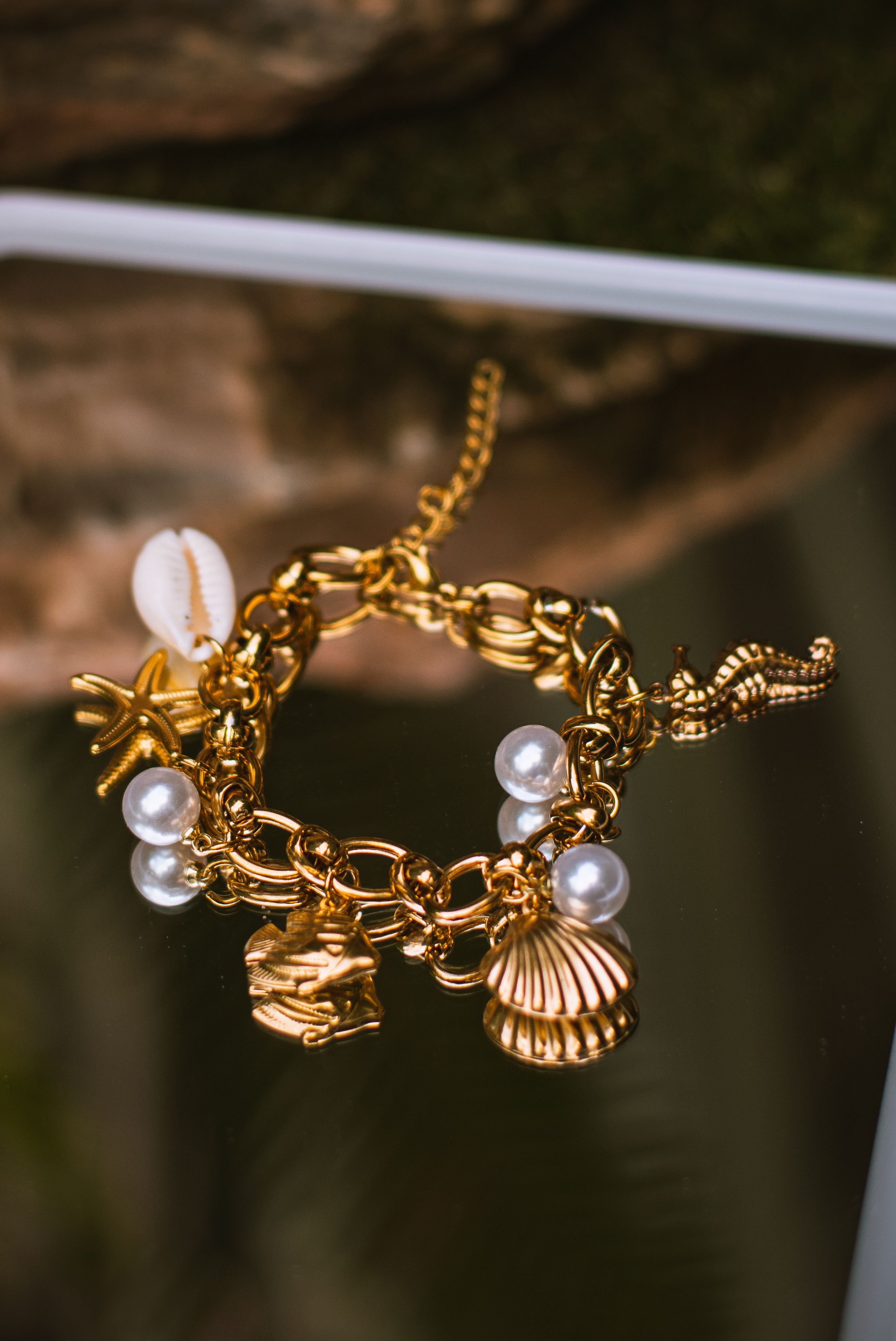 Luxurious gold charm bracelet adorned with pearls and seashell motifs, elegantly displayed.