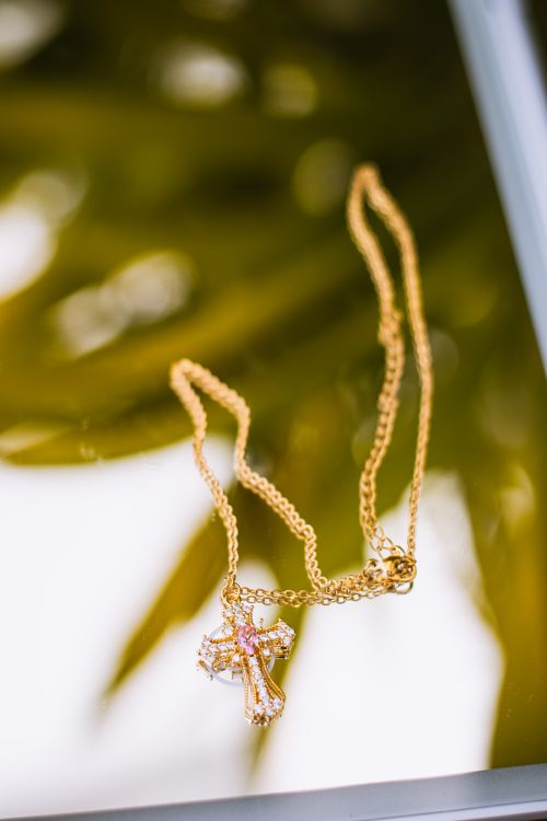 Free Close-up of a gold cross pendant necklace on reflective surface with a blurred background. Stock Photo