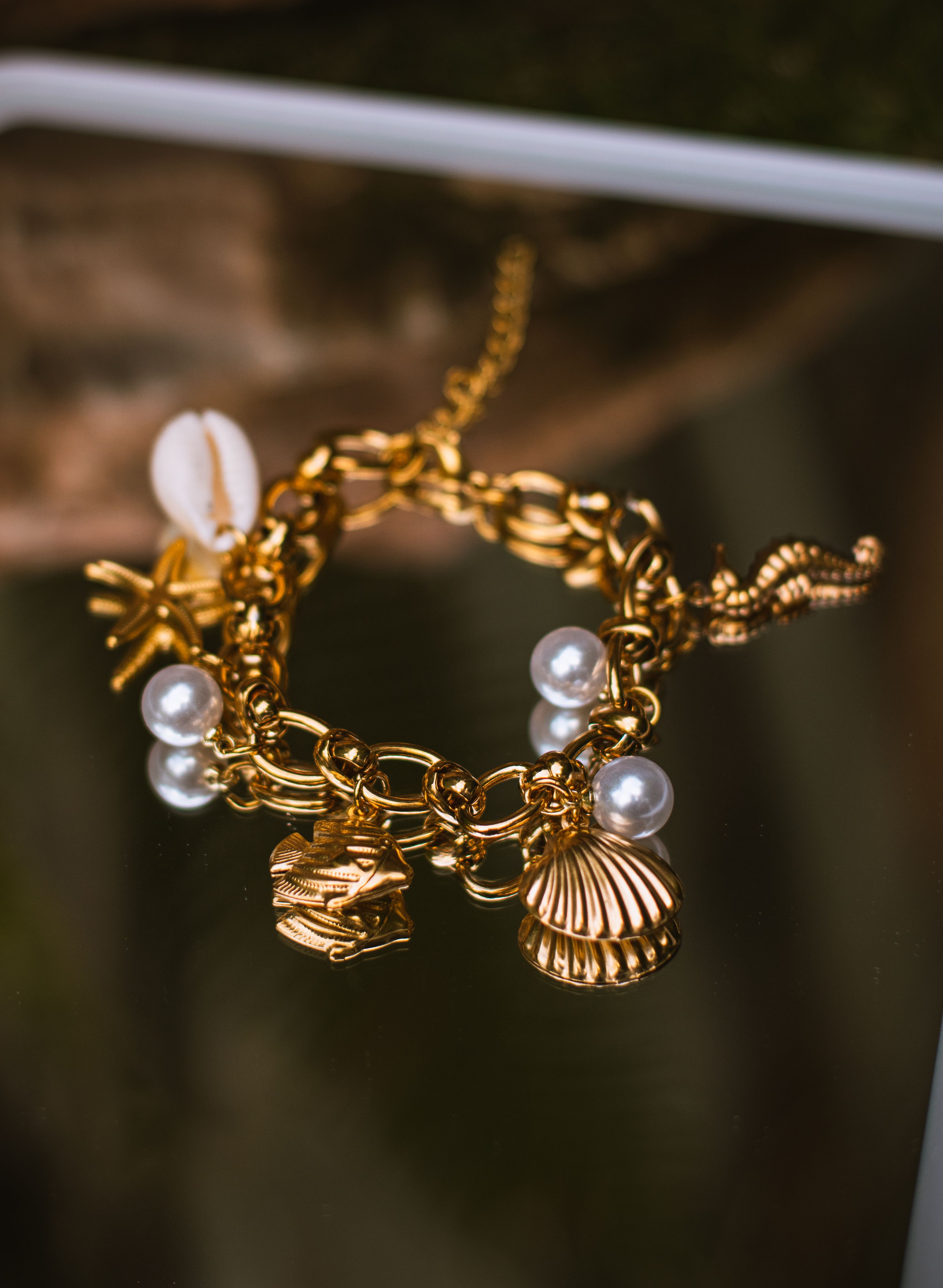 Golden charm bracelet with sea-themed charms and pearls on a reflective surface.