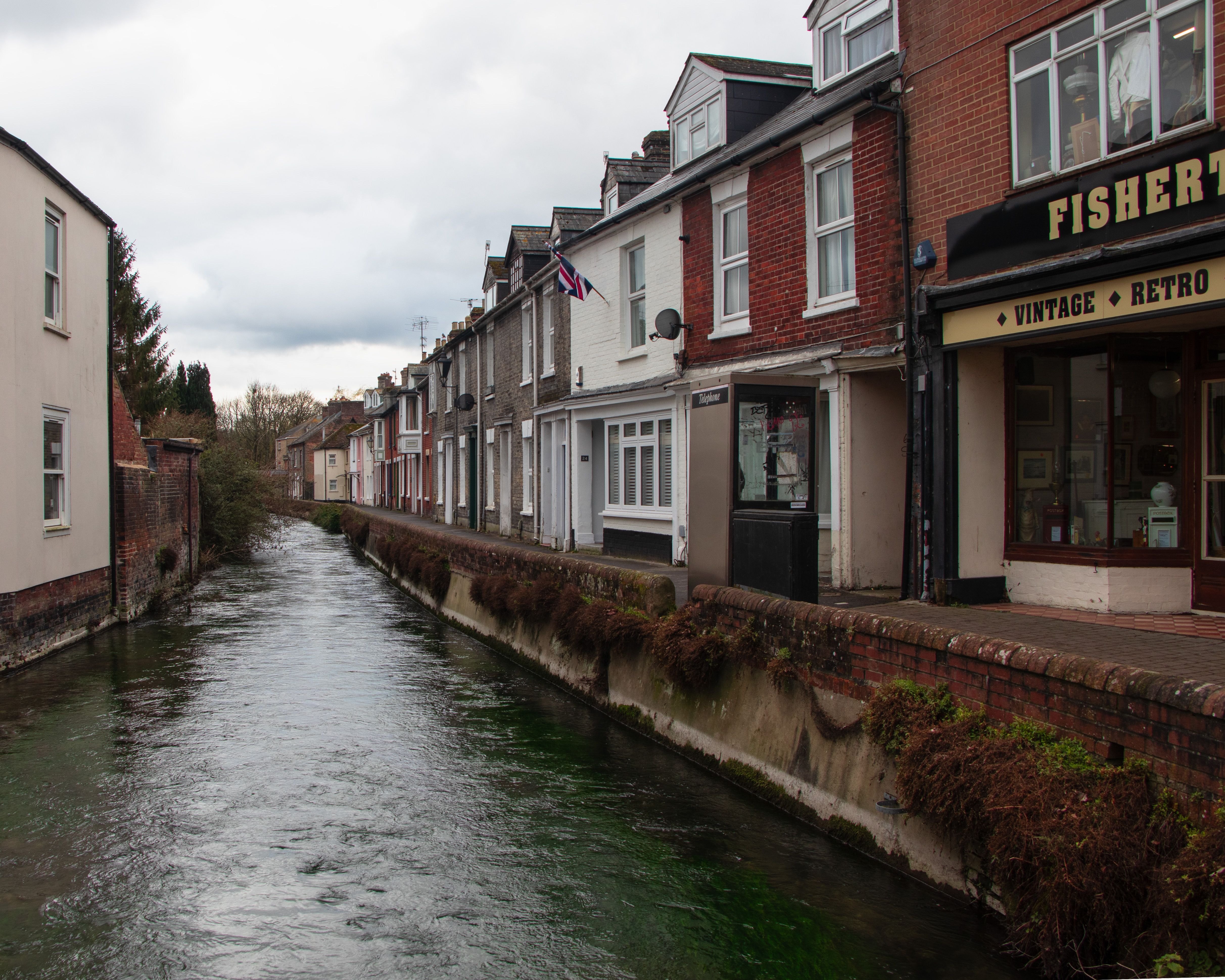 Picturesque canal street in England with vintage shop and row of houses under a clouded sky.