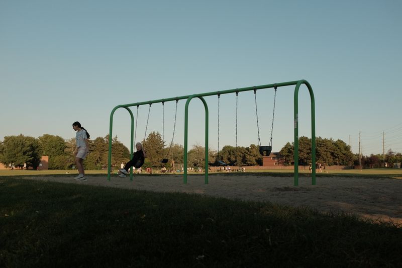 Two kids enjoy playing on swings in a sunny park setting.