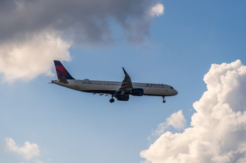 Free A Delta Air Lines airplane glides through a partly cloudy sky, offering a scenic view. Stock Photo