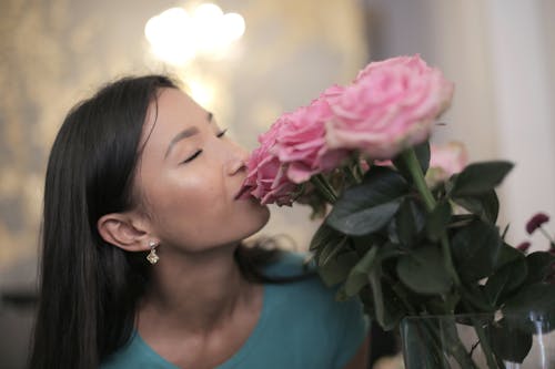 Woman in Blue Crew Neck T-shirt Smelling Pink Flowers