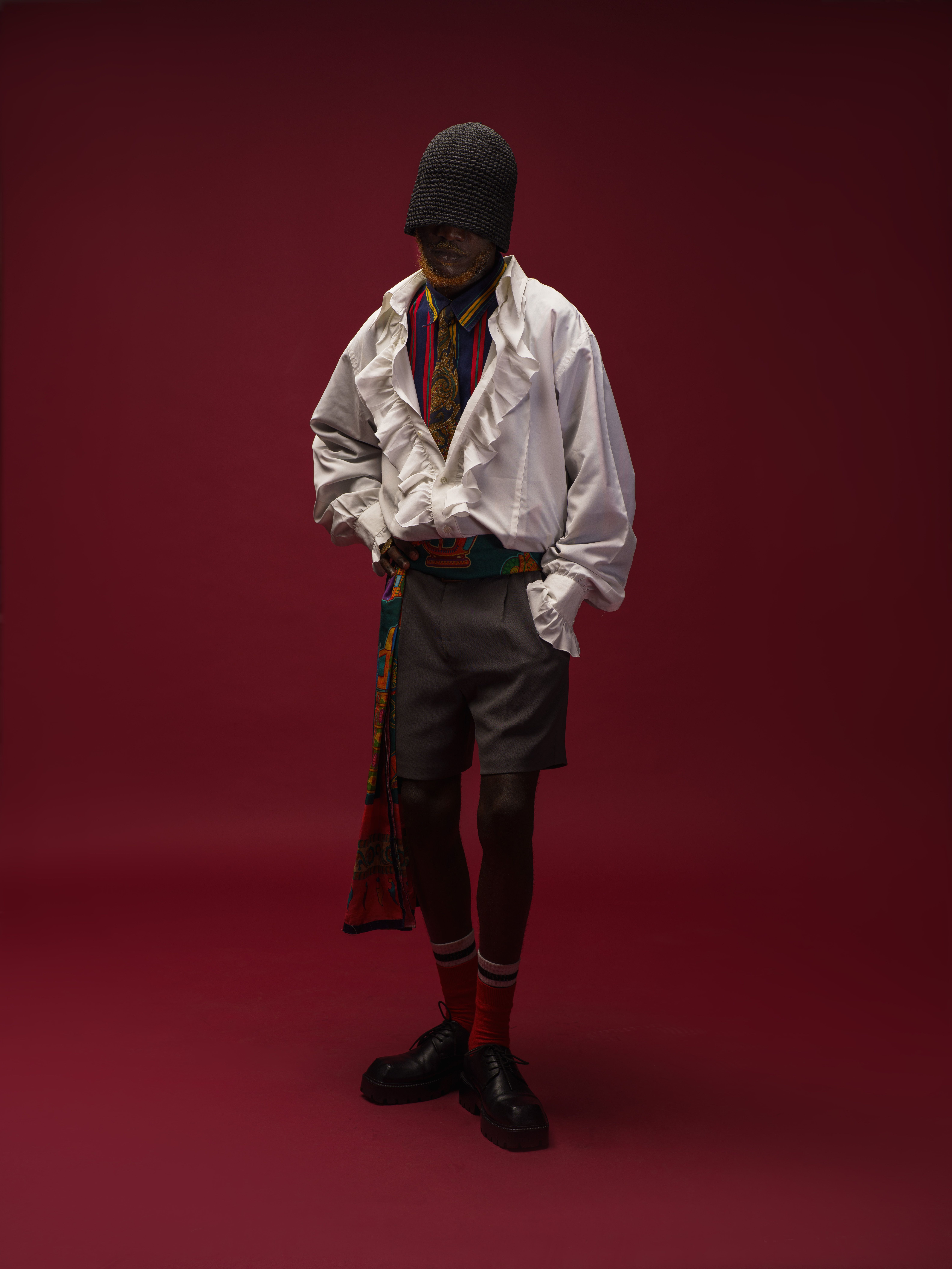 A man poses in vintage clothing against a bold red background.