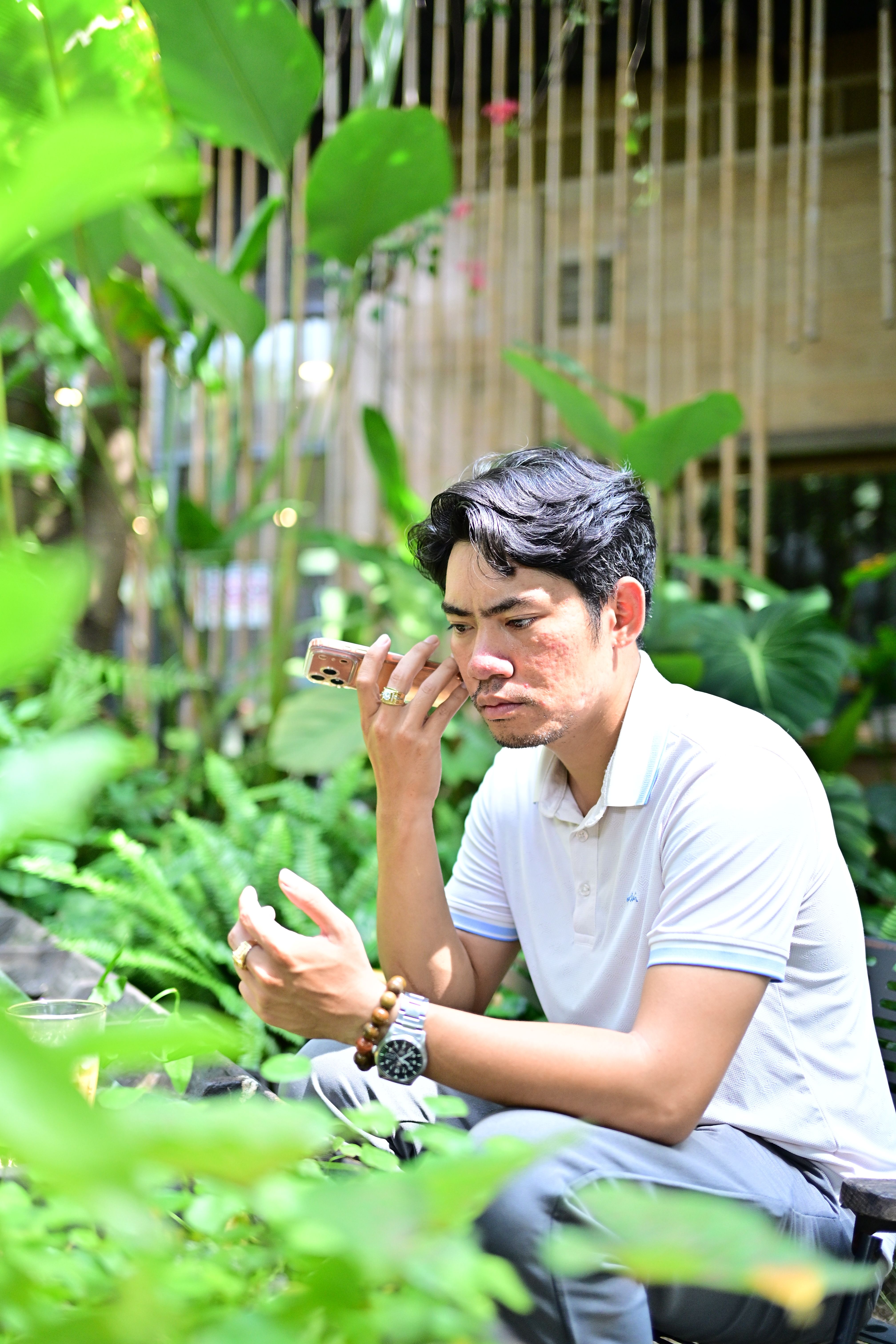 A man using a smartphone in a lush outdoor garden, surrounded by greenery and natural light.