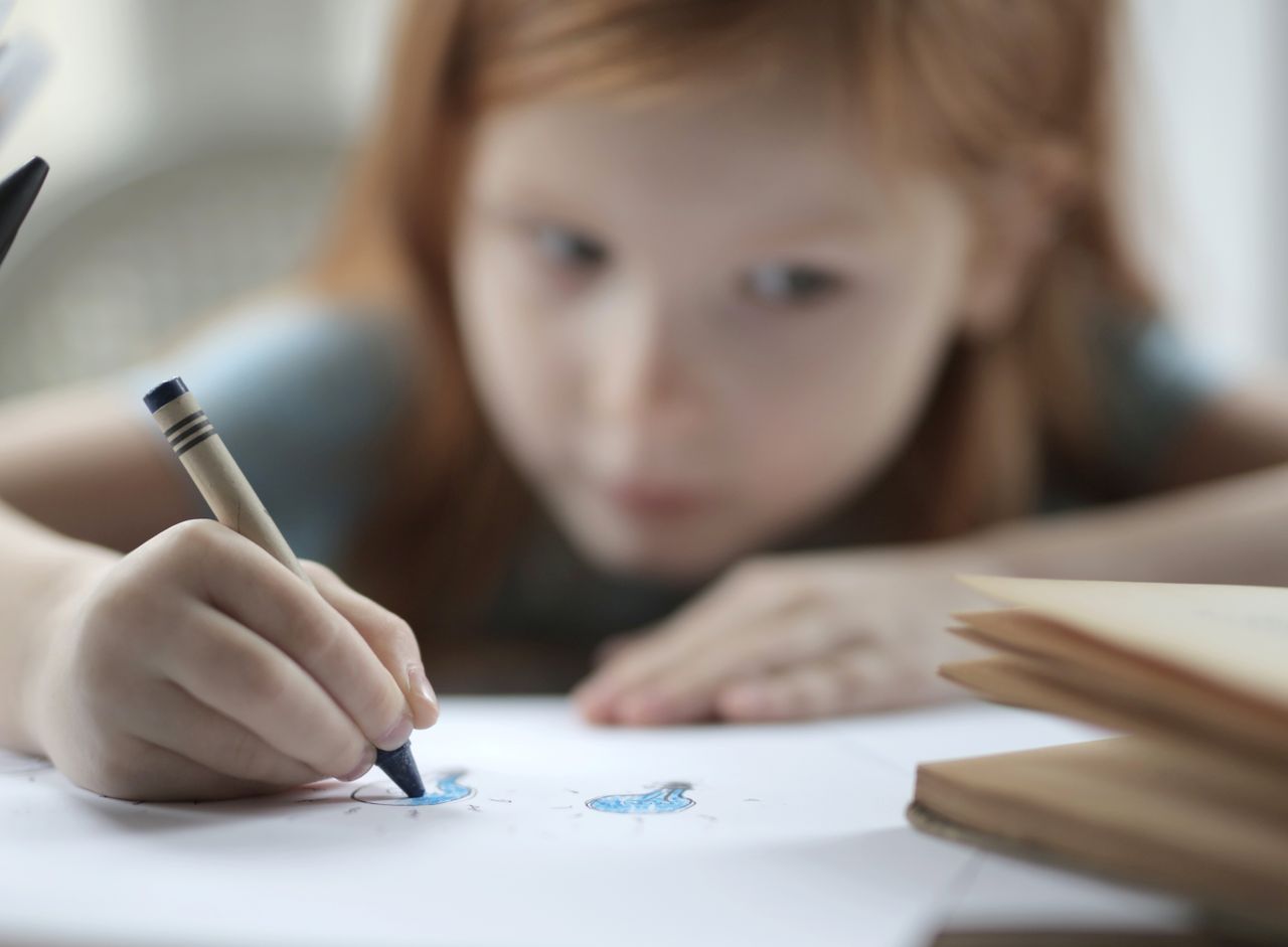 Seorang anak mewarnai gambar dengan krayon biru di kelas