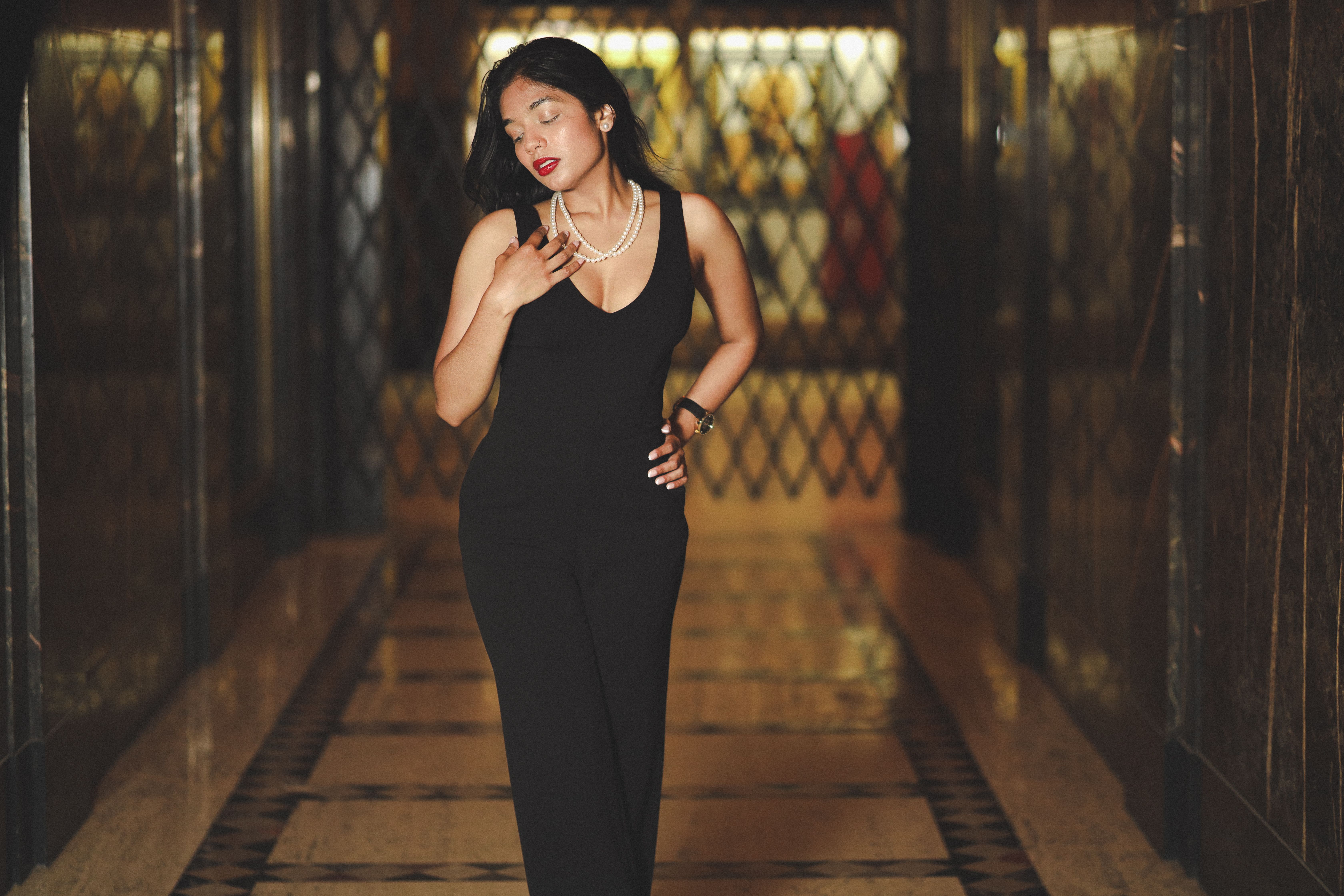 Sophisticated woman in black dress and pearls in an elegant hallway. Evening glamour.