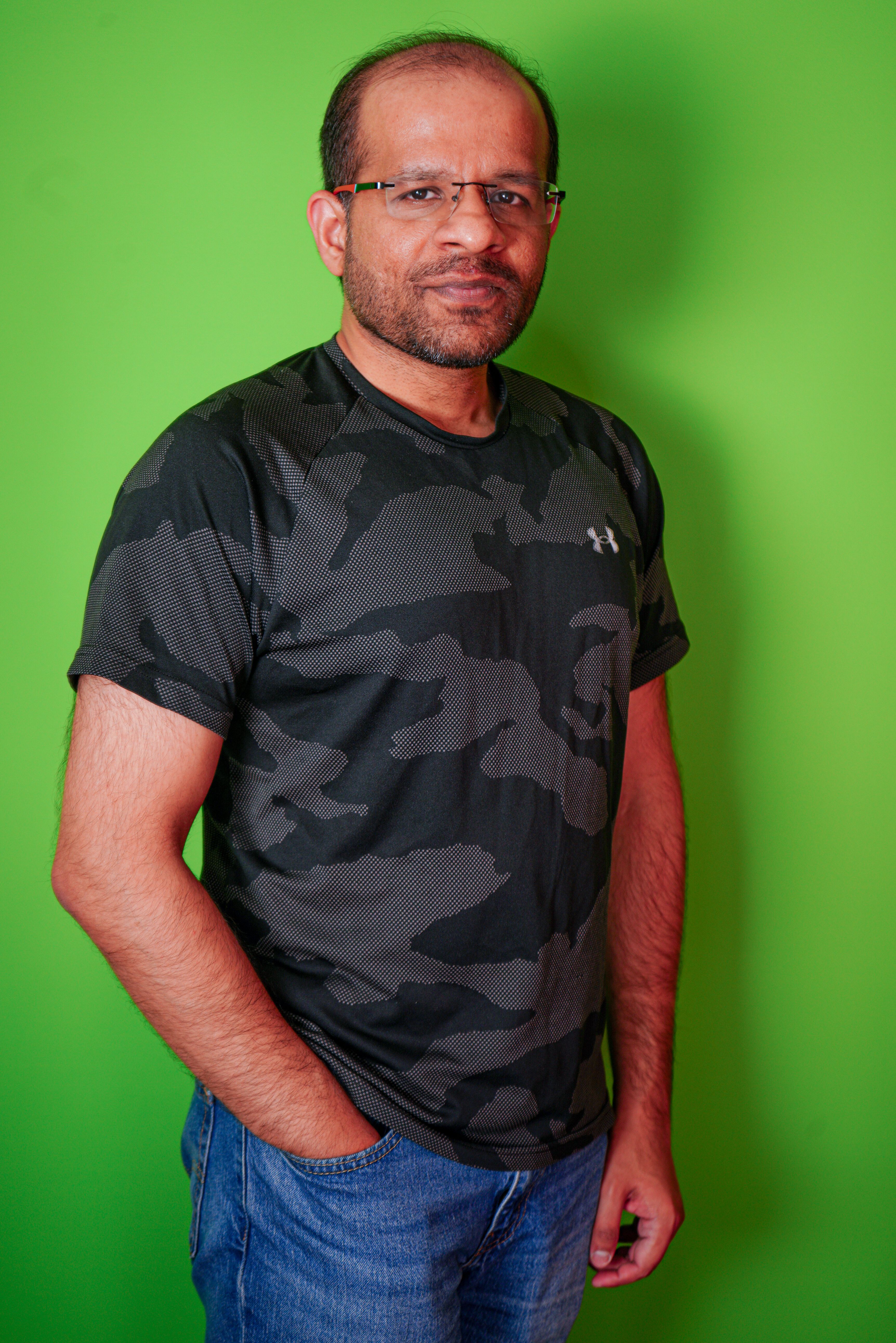 Casual portrait of a man wearing glasses and a camouflage shirt against a bright green backdrop.