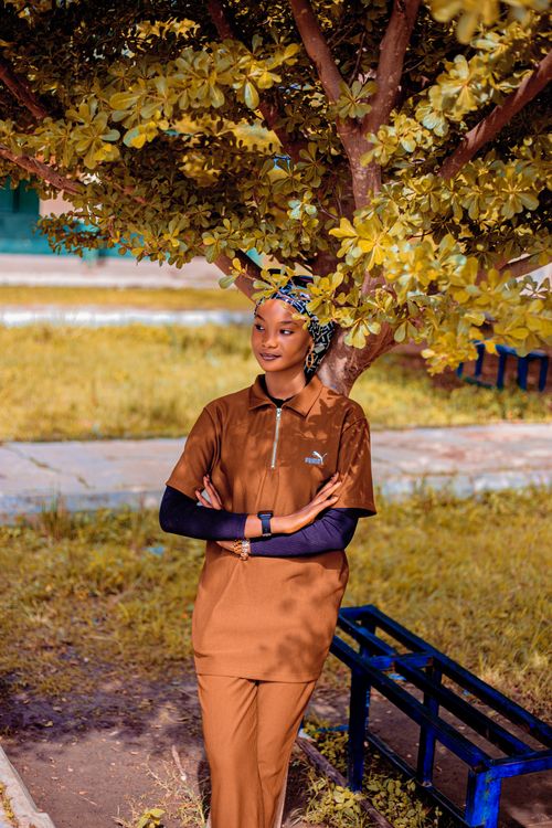 Free Woman in brown outfit standing under a tree in a garden. Bright, sunny day. Stock Photo