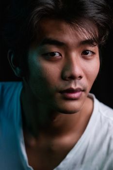 黑暗背景下，一位年轻的亚洲男子表情严肃的特写肖像