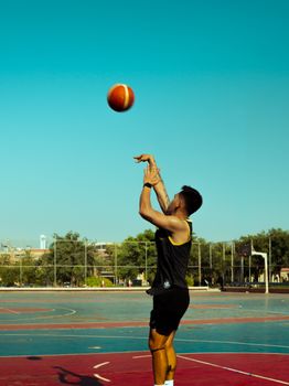 A young man taking a basketball shot on an outdoor court in Kuwait.