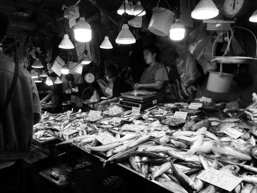 Free Black and white photo capturing a bustling fish market with vendors and a variety of fish on display. Stock Photo