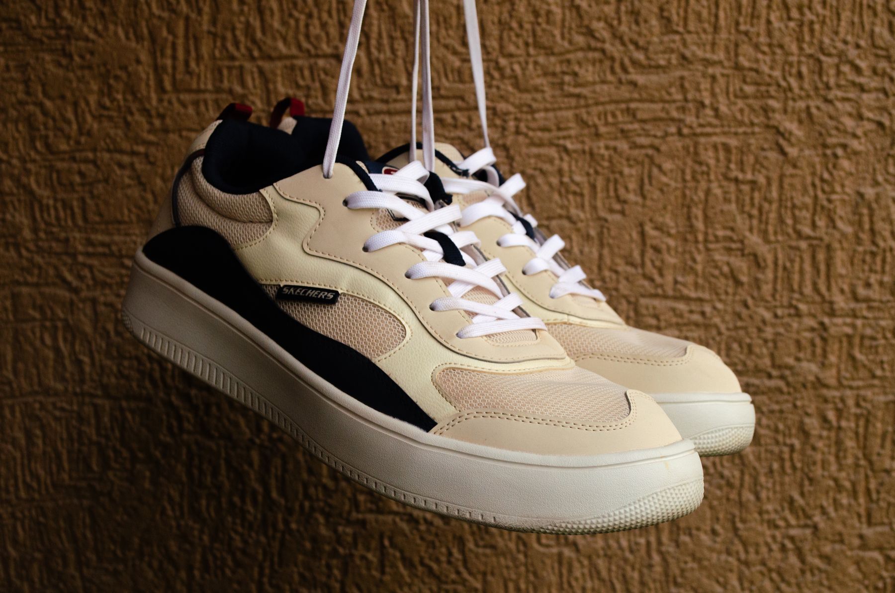Beige and black tonal sneakers hanging by their laces