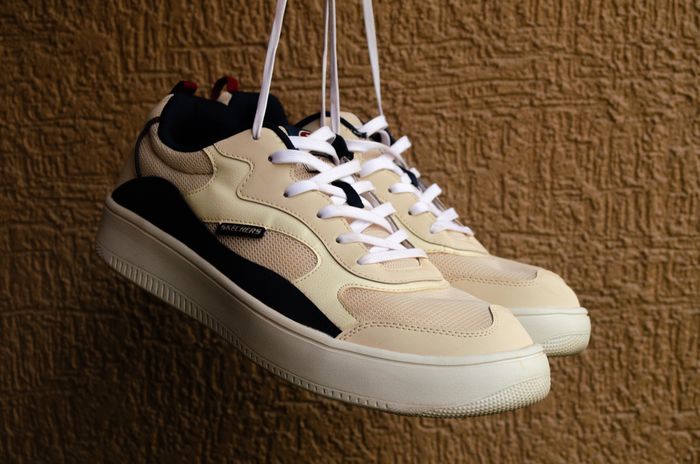 Stylish beige sneakers hanging against a textured wall — photo by Risiii on Pexels
