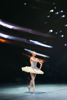 Graceful ballerina in white tutu performing under stage lights.
