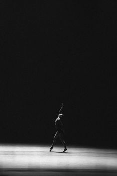 Elegant dancer highlighted in a dramatic spotlight on a minimalist stage.