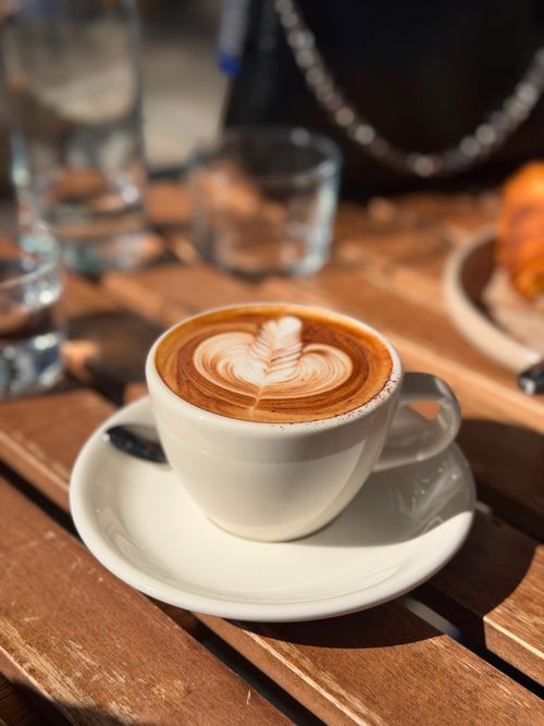Free A beautifully crafted latte with leaf art on a wooden table, bathed in warm sunlight. Stock Photo