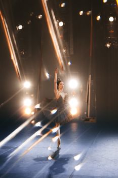 A graceful ballet dancer in a dramatic pose on a dimly lit stage with vibrant lighting effects.