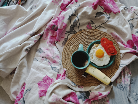 Top-view of breakfast with coffee, eggs, and tomato on floral fabric.