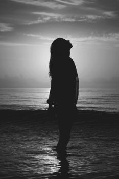 Silhouette of a woman standing on the beach at sunset, embracing the serene ocean view.