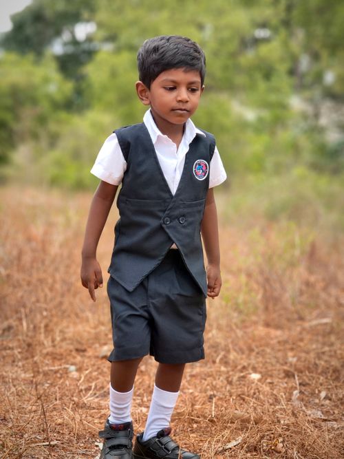 Free A young Indian boy in a school uniform, outdoors in a natural setting, walking thoughtfully. Stock Photo