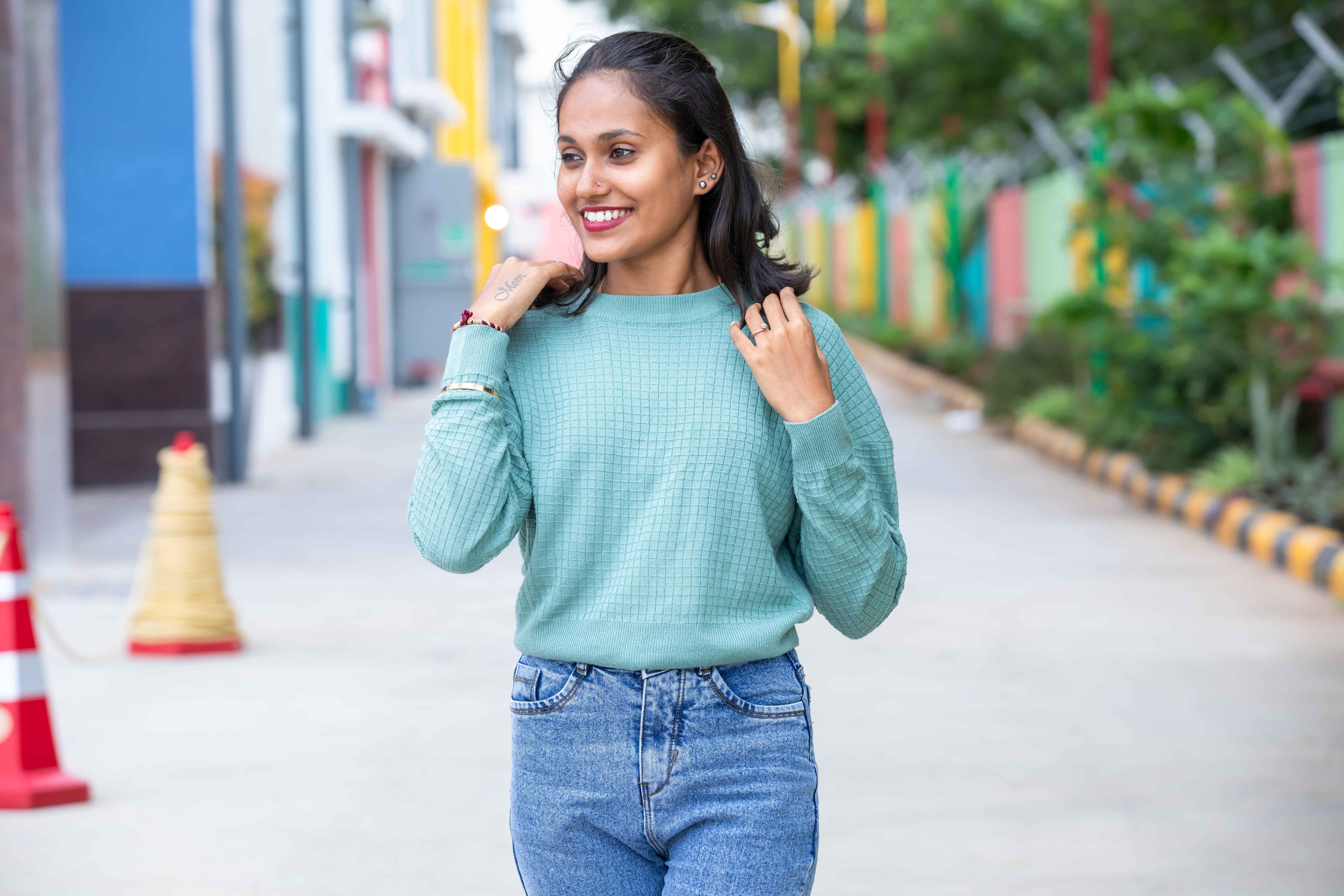 Young woman wearing casual outfit, smiling while walking on a colorful city street.