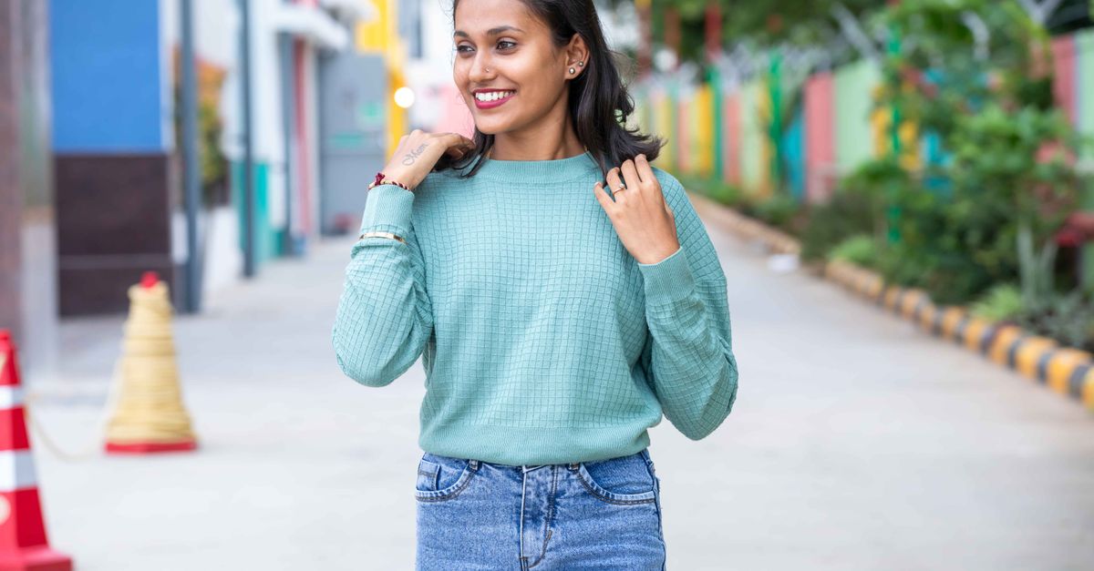 Young woman wearing casual outfit, smiling while walking on a colorful city street.