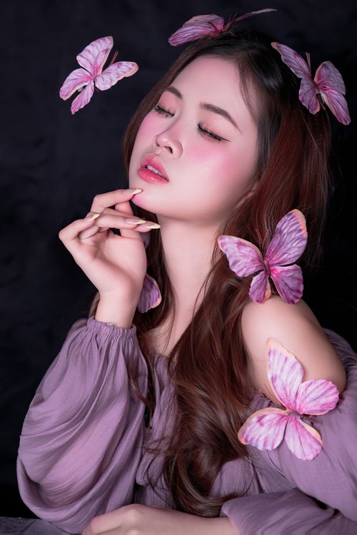 Free Woman posing with pink butterflies, showing a serene expression and soft lighting. Stock Photo