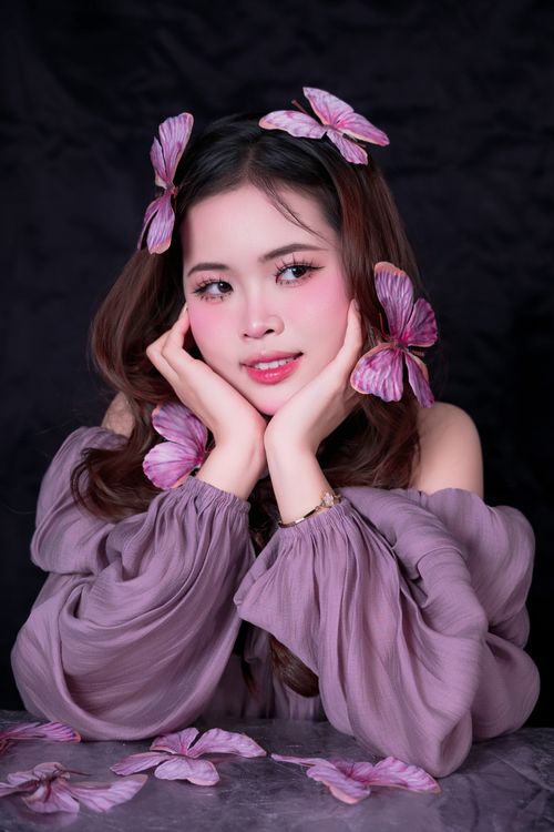 Free A beautiful woman with delicate pink flower accents poses gracefully in a purple dress against a dark background. Stock Photo