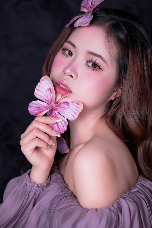 Free Artistic portrait of a young woman holding a pink butterfly, featuring a dreamy expression. Stock Photo